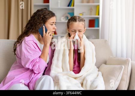 Mère attentionnée appelant le médecin tandis que sa fille malade se mouche à la maison Banque D'Images