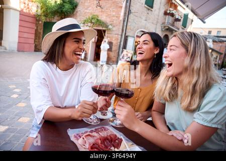 Trois amies joyeuses grillent avec du vin rouge au restaurant en plein air Banque D'Images