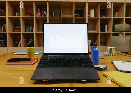 Ordinateur portable avec écran vierge sur un bureau en bois dans une bibliothèque moderne Banque D'Images