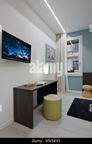 Chambre à coucher dans un appartement résidentiel converti d'anciens bureaux, avec un bureau pont, un pouf et une fenêtre avec rideau. Banque D'Images