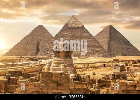La Grande Sphinx de Gizeh avec les célèbres pyramides de Khéops, Khéphren et Menkaourê en arrière-plan sous un ciel désertique dramatique au coucher du soleil, Égypte Banque D'Images