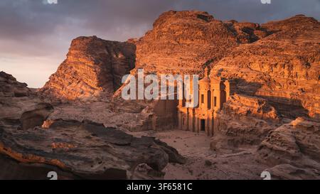 Vue panoramique large et majestueuse du monastère Ad Deir taillé dans les falaises de canyon en grès rouge à l'heure dorée du coucher du soleil dans l'antique Petra, Jordanie Banque D'Images