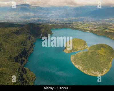 Vue aérienne de la Laguna de Cuicocha avec ses îles, entourée de pentes volcaniques vertes luxuriantes et de chaînes de montagnes lointaines sous un ciel nuageux Cotacachi, Banque D'Images