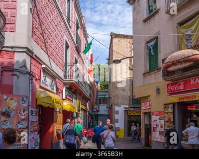 Les gens se promènent dans une rue étroite et vibrante bordée de bâtiments colorés et de diverses boutiques, dont des pizzerias et des stands de sandwichs. Banque D'Images