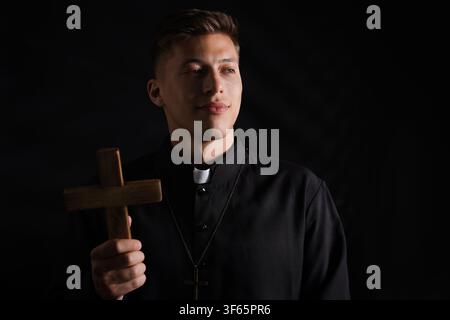 Prêtre avec croix en bois sur fond noir Banque D'Images