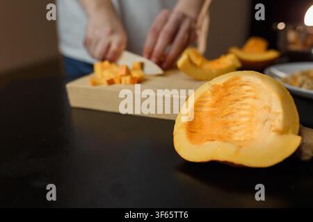Femme coupant un potiron sur une planche de cuisine, seules les mains visibles. Légumes de saison d'automne à cuisiner. Habitudes alimentaires saines, concept de nourriture végétarienne biologique Banque D'Images
