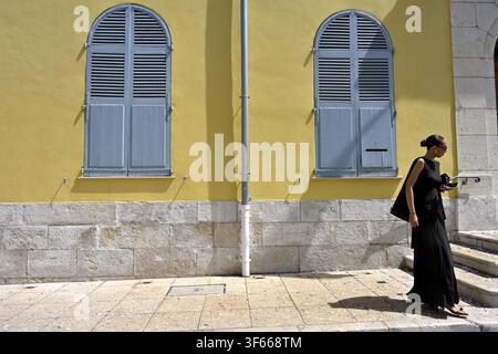 Femme élégante en robe noire devant un bâtiment jaune aux fenêtres cintrées fermées Banque D'Images