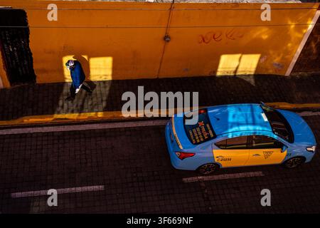 Cholula, Puebla, Mexique, 27 septembre 2022. Un piéton marche à côté d'un taxi local sur une rue ensoleillée vue du dessus Banque D'Images
