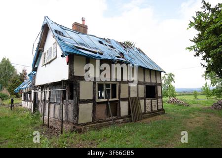 Un cottage Tudor en bois délabré en cours de restauration structurelle avec une bâche bleue endommagée sur le toit dans le Herefordshire. Banque D'Images