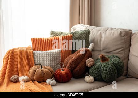 Disposition de coussins en forme de citrouille en peluche et de coussins tricotés doux dans des tons chauds automnaux créant une ambiance accueillante. Une lumière naturelle douce met en valeur Banque D'Images