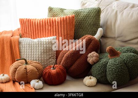 Diverses coussins décoratifs en peluche en forme de citrouilles et coussins moelleux texturés dans des tons orange et crème disposés sur un canapé. Une lumière douce et diffuse met en valeur le tissu Banque D'Images