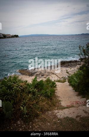 Vue panoramique de marches de pierre descendant vers la côte rocheuse avec des cactus et des îles lointaines sous un ciel nuageux Banque D'Images