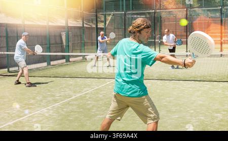 Hommes adultes jouant au padel contre deux hommes Banque D'Images