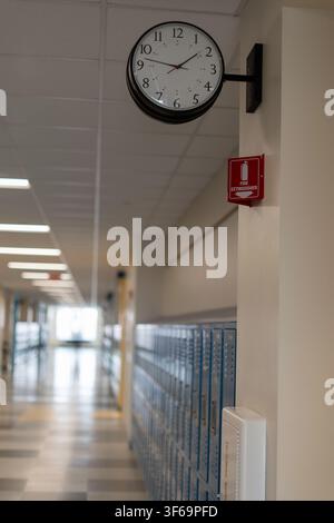 Une vue en perspective d'un couloir d'école propre et moderne présentant une horloge ronde montée sur un pilier, un équipement d'urgence et une longue rangée de métal bleu Banque D'Images