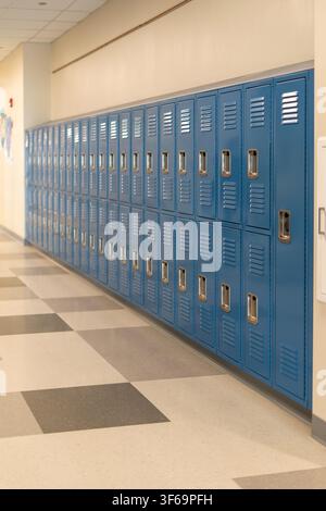 Une photographie en perspective grand angle montrant une rangée étendue de casiers en métal bleu bordant le mur d'un couloir d'école propre avec un motif moderne Banque D'Images