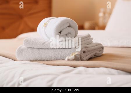 Pile de serviettes blanches propres avec une fleur décorative sur un lit d'hôtel, concept d'hospitalité et de confort, cet arrangement suggère une expérience spa relaxante Banque D'Images