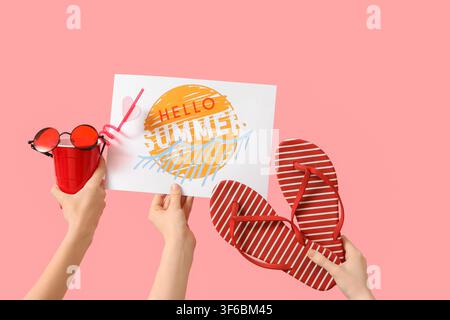 Mains tenant paire de tongs, papier avec texte HELLO SUMMER et accessoires de plage sur fond rose Banque D'Images