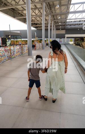 Mère tenant la main de son fils en marchant dans un centre commercial intérieur lumineux Banque D'Images