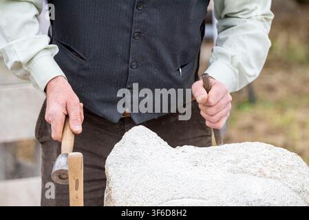 Un travail manuel traditionnel montrant un homme frappant un burin en métal pour façonner une pierre lourde lors d'une foire historique Banque D'Images