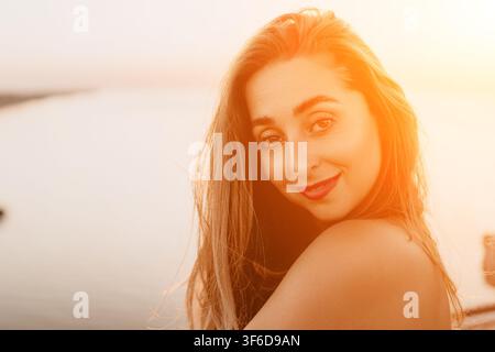 Portrait de femme au coucher du soleil, belle jeune femme souriant tout en regardant par-dessus son épaule sur la plage pendant le coucher du soleil Banque D'Images