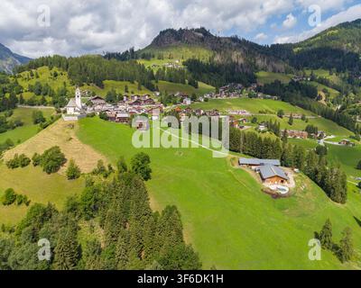 Vue aérienne du village alpin niché dans les pentes verdoyantes des Dolomites avec des maisons traditionnelles et une église historique à Colle Santa Lucia Banque D'Images