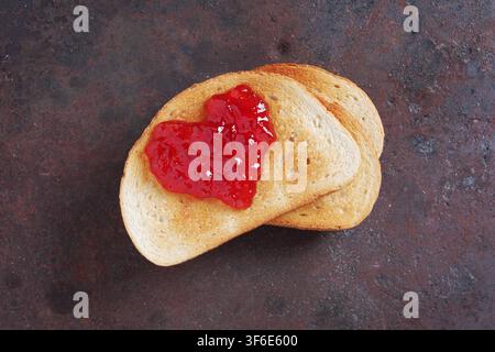 Confiture de fraises en forme de cœur sur une tranche de pain grillé sur un fond métallique usé, vue de dessus Banque D'Images