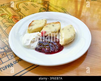 Cuisine régionale russe authentique. Lapuny au fromage frais traditionnel de Smolensk cuits au four, servis avec une confiture de canneberge douce et acide et une riche crème fraîche sur w Banque D'Images