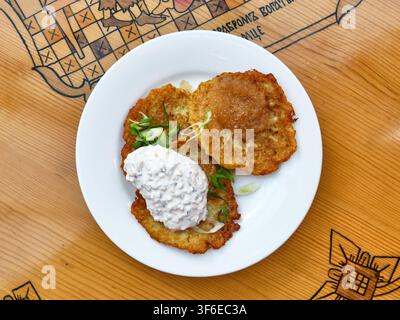 Vue de dessus de pancakes de pommes de terre dorés et croustillants biélorussiens draniki servis avec du caviar de brochet de qualité supérieure, une sauce crémeuse et des oignons verts frais sur une assiette sur wo Banque D'Images
