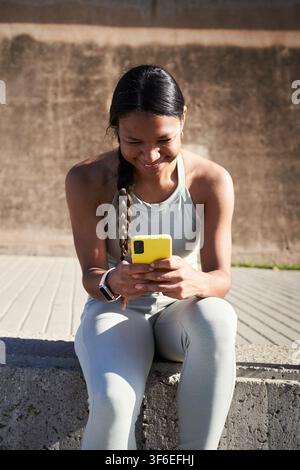 Athlète noire latine souriante utilisant un smartphone pendant une pause d'entraînement en plein air Banque D'Images