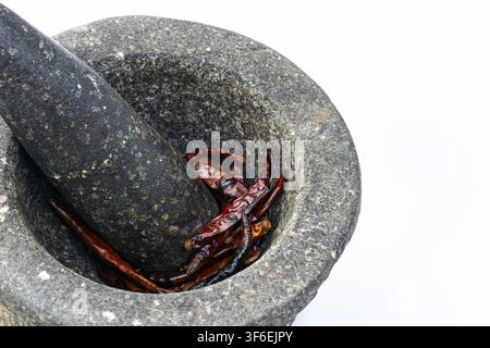 Mortier et pilon traditionnels en pierre lourde remplis de piments rouges séchés, isolés sur fond blanc, un outil de broyage authentique de la cuisine thaïlandaise. Banque D'Images