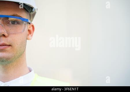 Visage recadré d'un ingénieur en construction portant un équipement de sécurité sur fond clair. Recrutement d'entreprise et portrait de profession ingénieur. Banque D'Images
