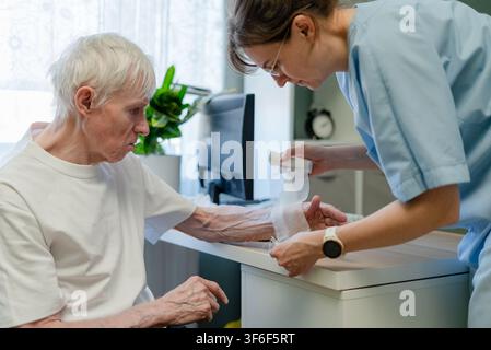 Infirmière traitant la main d'un homme âgé dans une clinique dermatologique. Professionnel de santé fournissant des soins dermatologiques gériatriques et un traitement de la peau vieillissante pour un patient âgé lors d'un examen médical approfondi dans le bureau Banque D'Images