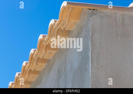 Vue rapprochée de tuiles de terre cuite érodées et d'un mur en stuc texturé sous un ciel bleu éclatant Banque D'Images