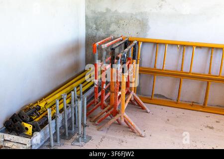 Divers matériaux de construction, y compris des poteaux télescopiques jaunes, des supports ajustables orange et noir et des châssis d'échafaudage jaunes, sont organisés et r Banque D'Images