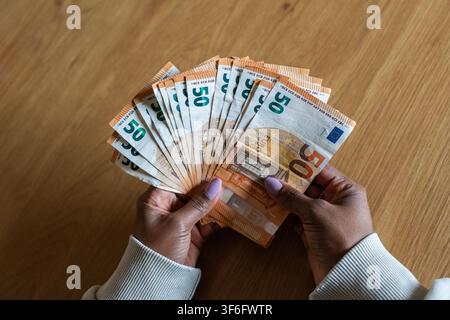 Femme noire comptant des billets de cinquante euros sur une table en bois Banque D'Images