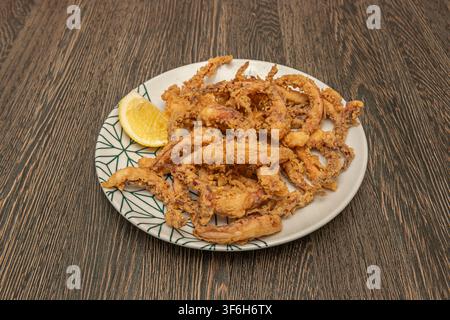 Morilles de calmar frites dorées empilées avec une tranche de citron, servies sur une assiette à motifs sur une table en bois sombre Banque D'Images