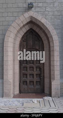 Tachkent, Ouzbékistan – 12 avril 2026 – Vue frontale en gros plan d'une lourde porte en bois gothique encadrée dans une arche en pierre. Banque D'Images