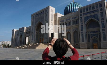 Tachkent, Ouzbékistan - 18 avril 2026 - Un visiteur photographie la coupole détaillée de la mosquée et le travail de tuiles sur la façade d'un bâtiment islamique historique. Banque D'Images