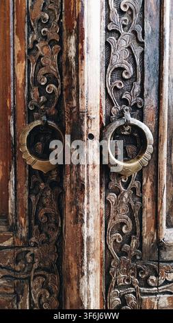 Tachkent, Ouzbékistan - 18 avril 2026 - Détail de porte en bois avec des sculptures florales complexes et des poignées en anneaux métalliques, artisanat classique et traditionnel Banque D'Images