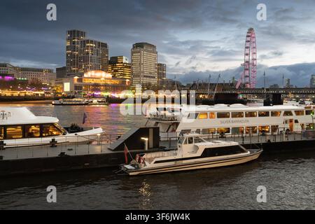 Les bateaux fluviaux accostent au quai de Woods sur la Tamise au crépuscule, avec le London Eye et la Royal Festival Hall illuminés sur la rive sud. Banque D'Images