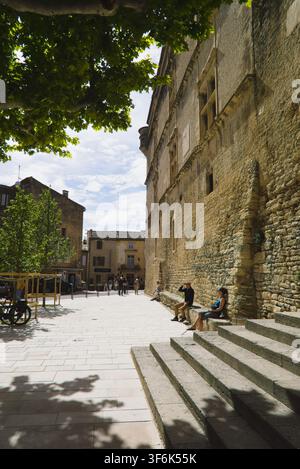 Touristes se reposant sur des bancs en pierre le long des remparts dans la place ensoleillée de Gordes, Provence, France. Banque D'Images
