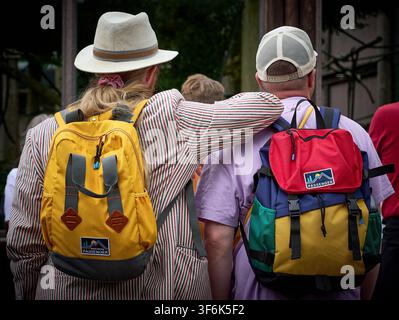 Vue arrière de deux amis avec un bras autour de l'autre, portant des sacs à dos colorés et des chapeaux en plein air Banque D'Images