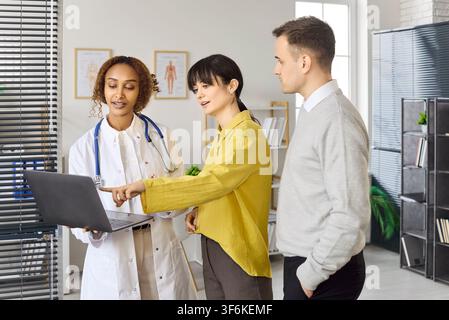 Couple examinant les résultats avec un médecin en utilisant un ordinateur portable lors d'une consultation de planification de la fertilité Banque D'Images