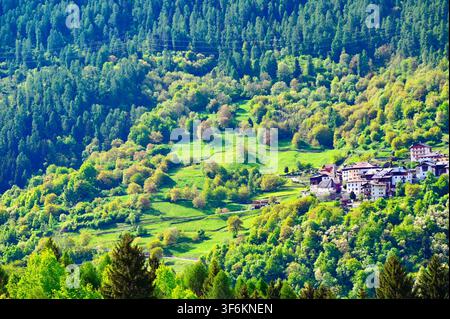 Photographie de paysage de style aérien horizontal d'un petit village isolé niché sur une pente montagneuse verdoyante et arborée, entouré de forêts denses. Banque D'Images