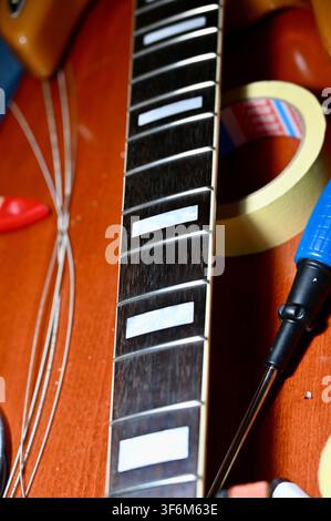 Photographie verticale en gros plan d'un touche de guitare mettant l'accent sur les cordes métalliques et les incrustations blanches rectangulaires de positionnement, sur un corps d'instrument en bois flou, mettant en valeur les détails et la texture Banque D'Images