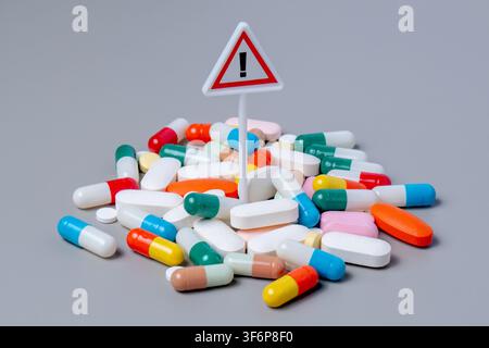 Panneau d'avertissement debout dans un tas dense de pilules colorées en capsules. Risque de médication et effets secondaires, concept de surdose de drogue. Banque D'Images
