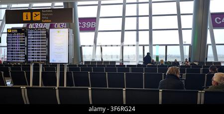 Zone d'attente des portes d'embarquement avec écrans d'informations de vol, panneaux des portes C39A et C39B, rangées de sièges pour les passagers et vues sur le tarmac à travers la fenêtre du terminal Banque D'Images