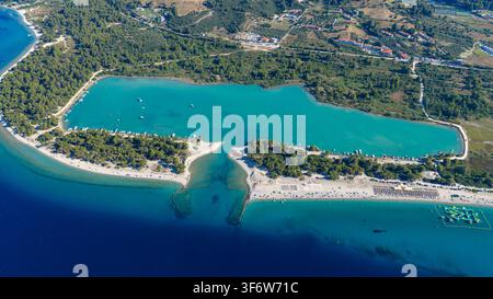 Une eau turquoise claire remplit une lagune côtière à côté de plages de sable, d'une ligne de côte boisée, de bateaux ancrés et de maisons dispersées sur la côte grecque. Banque D'Images