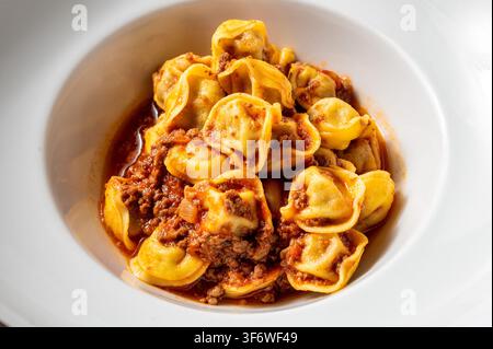 Tortellini italiennes servi avec une riche ragù de bœuf et une sauce tomate, présenté dans un bol en céramique blanche. Plat de pâtes fait maison traditionnel d'Italie centrale. Banque D'Images