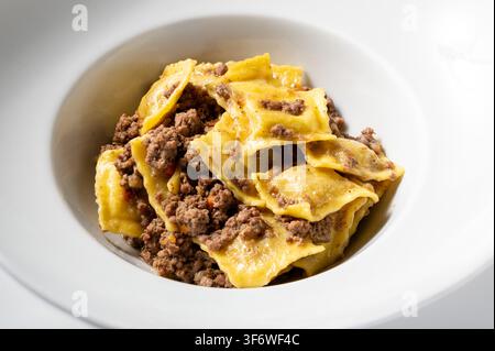Raviolis italiens farcis à la viande et servis avec un riche ragù traditionnel au bœuf, présentés dans un bol en céramique blanche. Plat de pâtes fait maison classique. Banque D'Images